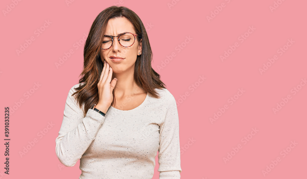 Young brunette woman wearing casual clothes and glasses touching mouth with hand with painful expression because of toothache or dental illness on teeth. dentist Young brunette woman wearing casual clothes and glasses touching mouth with hand with painful expression because of toothache or dental illness on teeth. dentist