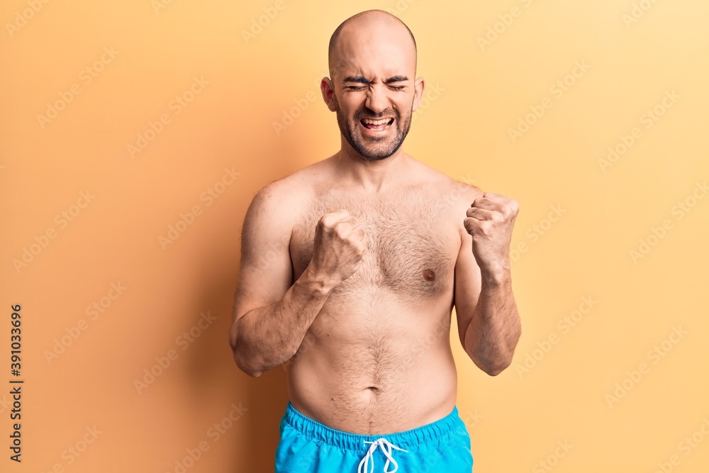 Young handsome bald man wearing swimwear shirtless celebrating surprised and amazed for success with arms raised and eyes closed