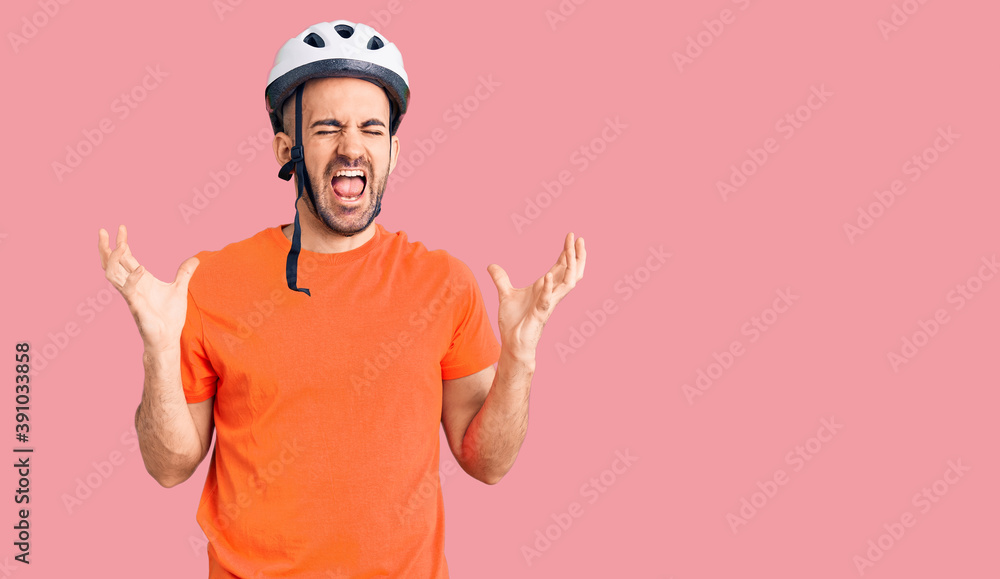 Young handsome man wearing bike helmet celebrating mad and crazy for success with arms raised and closed eyes screaming excited. winner concept Young handsome man wearing bike helmet celebrating mad and crazy for success with arms raised and closed eyes screaming excited. winner concept