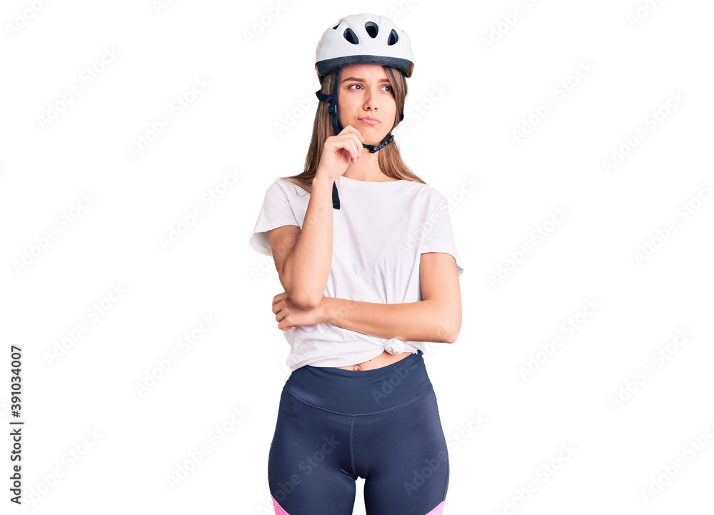 Young beautiful girl wearing bike helmet serious face thinking about question with hand on chin, thoughtful about confusing idea Young beautiful girl wearing bike helmet serious face thinking about question with hand on chin, thoughtful about confusing idea