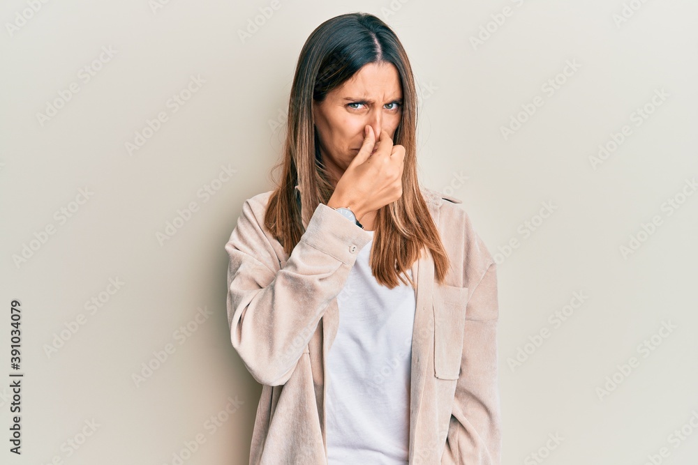 Brunette young woman wearing casual clothes smelling something stinky and disgusting, intolerable smell, holding breath with fingers on nose. bad smell Brunette young woman wearing casual clothes smelling something stinky and disgusting, intolerable smell, holding breath with fingers on nose. bad smell