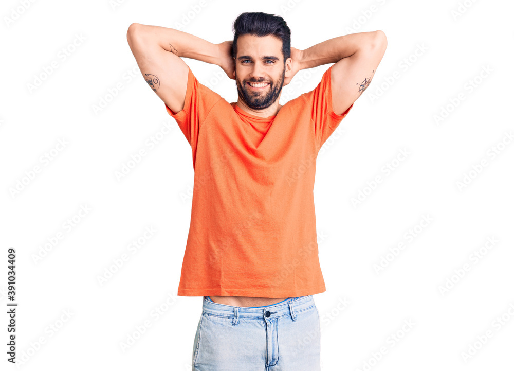 Young handsome man with beard wearing casual t-shirt relaxing and stretching, arms and hands behind head and neck smiling happy Young handsome man with beard wearing casual t-shirt relaxing and stretching, arms and hands behind head and neck smiling happy
