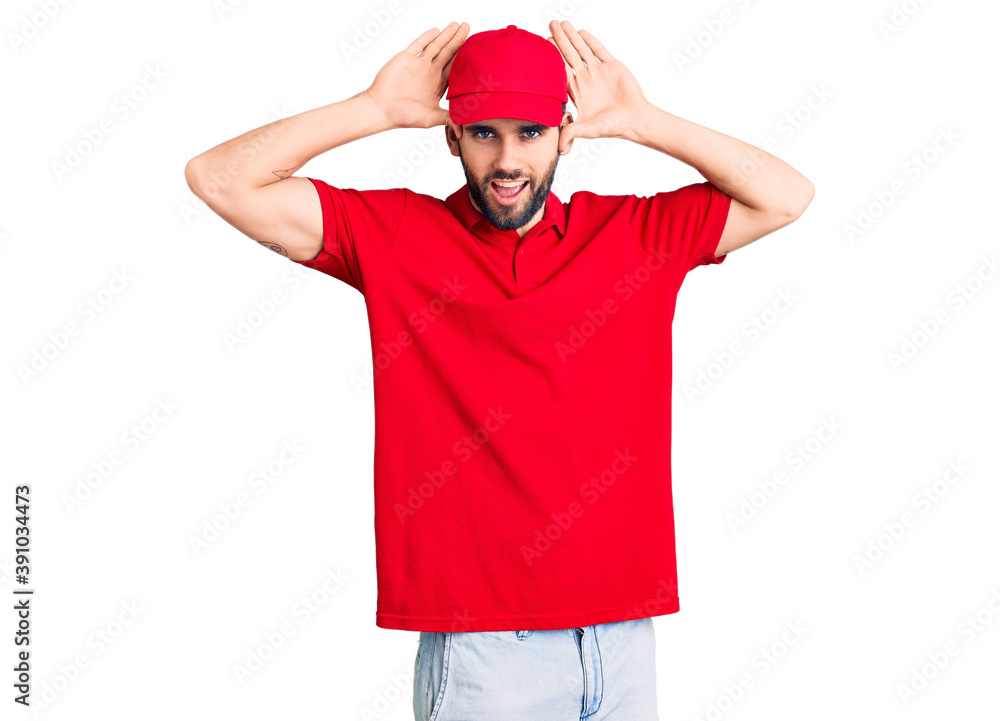 Young handsome man with beard wearing delivery uniform smiling cheerful playing peek a boo with hands showing face. surprised and exited