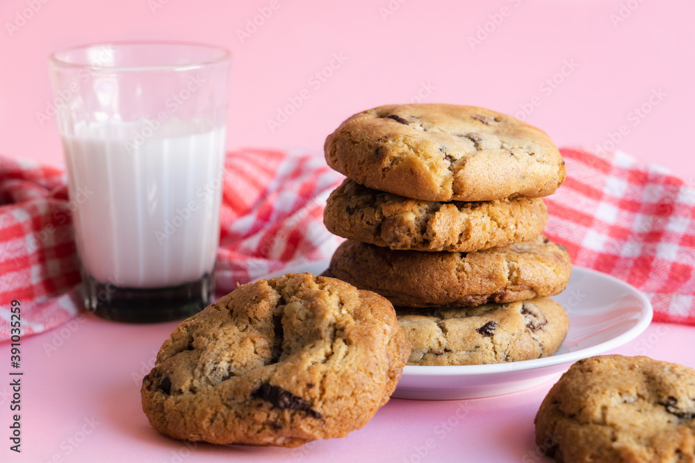 Stack of chocolate chip cookies beside a glass of milk in front of a pink background Stack of chocolate chip cookies beside a glass of milk in front of a pink background