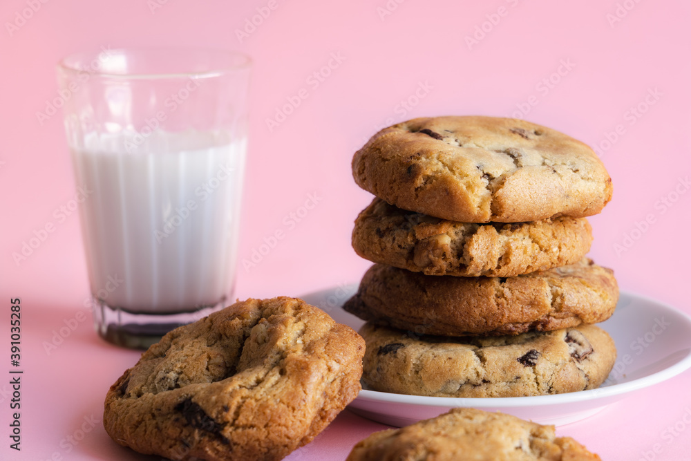 Stack of chocolate chip cookies beside a glass of milk in front of a pink background Stack of chocolate chip cookies beside a glass of milk in front of a pink background