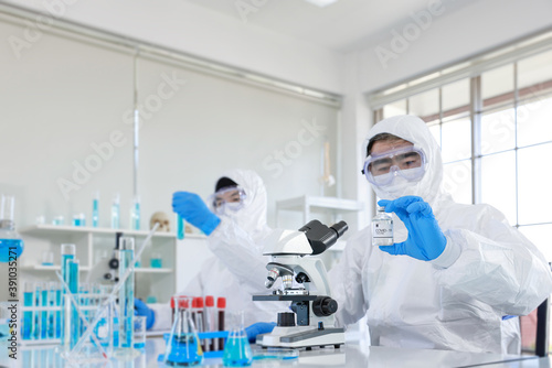 Healthcare professional in protective gloves and workwear holding & organising a tray of COVID-19 vaccine vials. The professional is carrying out researches on COVID-19 vaccine in laboratory.