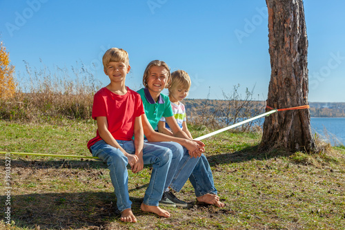 The boys sit on a rope stretched between trees against the backdrop of a picturesque lake.
