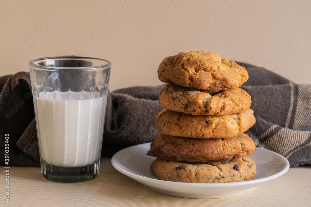 Stack of chocolate chip cookies beside a glass of milk in front of a beige background. Stack of chocolate chip cookies beside a glass of milk in front of a beige background.