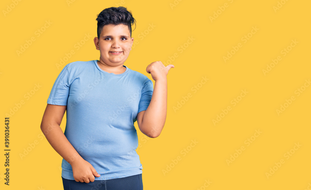 Little boy kid wearing sports workout clothes smiling with happy face looking and pointing to the side with thumb up. Little boy kid wearing sports workout clothes smiling with happy face looking and pointing to the side with thumb up.