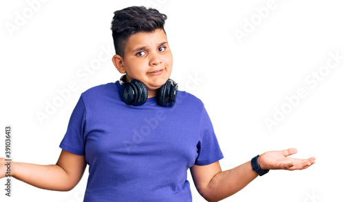 Little boy kid listening to music wearing headphones clueless and confused expression with arms and hands raised. doubt concept. © Krakenimages.com