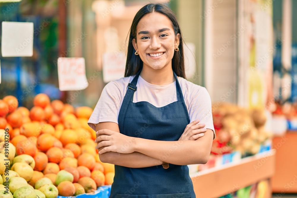 Φωτογραφία Young latin shopkeeper girl with arms crossed smiling happy at the fruit store