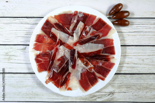 Portion of acorn-fed Iberian ham on white plate, on rustic wooden table