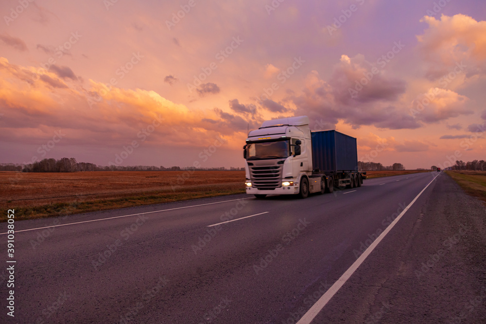 A mainline truck with a wagon goes along the highway against the backdrop of sunset clouds. A mainline truck with a wagon goes along the highway against the backdrop of sunset clouds.