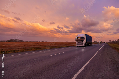 A mainline truck with a wagon goes along the highway against the backdrop of sunset clouds.