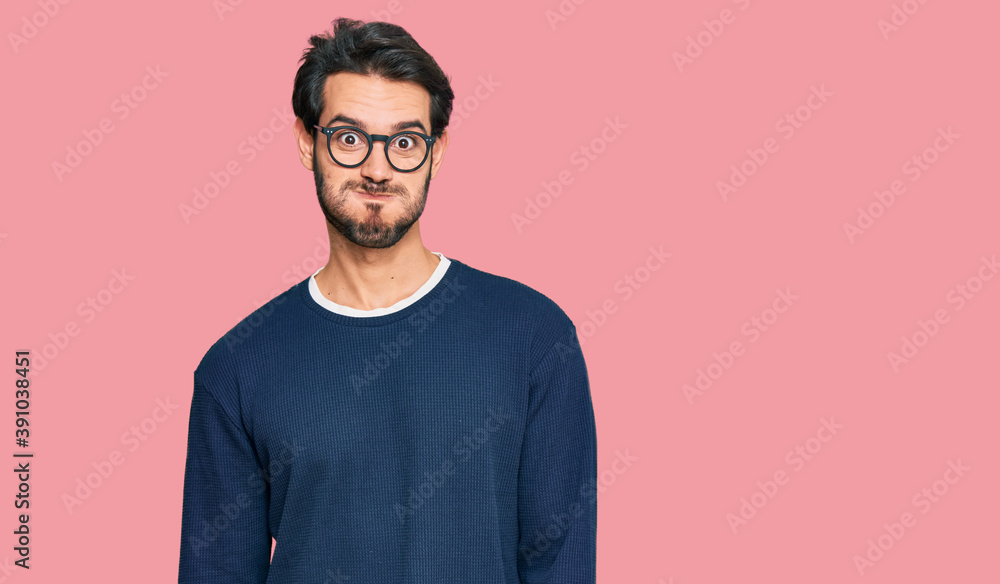Young hispanic man wearing casual clothes and glasses puffing cheeks with funny face. mouth inflated with air, crazy expression. Young hispanic man wearing casual clothes and glasses puffing cheeks with funny face. mouth inflated with air, crazy expression.