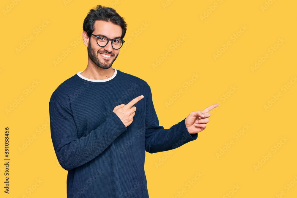 Young hispanic man wearing casual clothes and glasses smiling and looking at the camera pointing with two hands and fingers to the side. Young hispanic man wearing casual clothes and glasses smiling and looking at the camera pointing with two hands and fingers to the side.