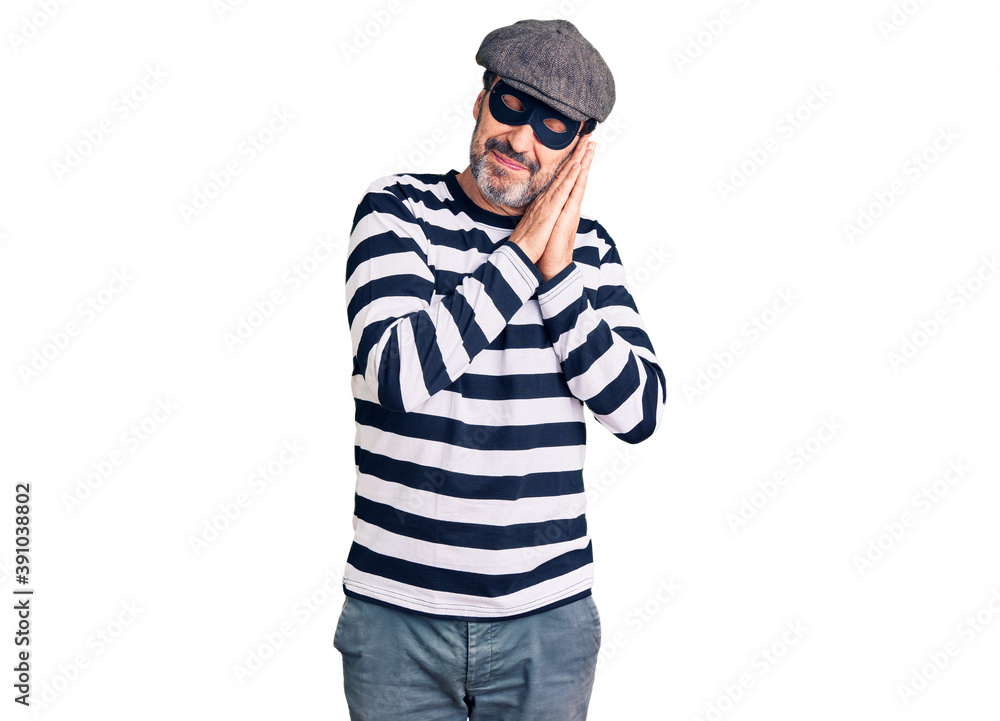 Middle age handsome man wearing burglar mask sleeping tired dreaming and posing with hands together while smiling with closed eyes. Middle age handsome man wearing burglar mask sleeping tired dreaming and posing with hands together while smiling with closed eyes.