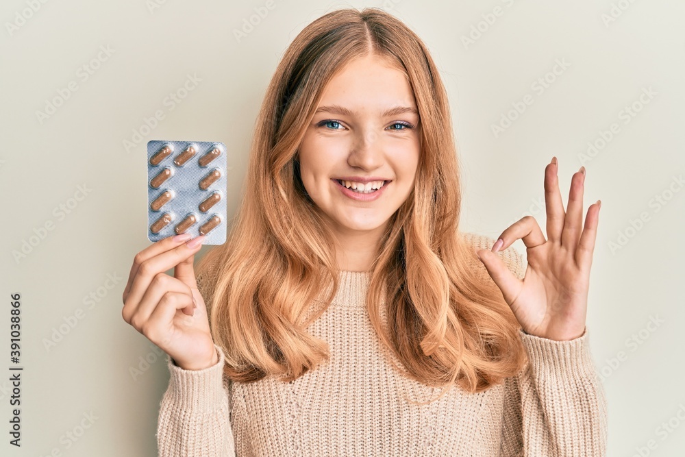 Beautiful young caucasian girl holding pills doing ok sign with fingers, smiling friendly gesturing excellent symbol Beautiful young caucasian girl holding pills doing ok sign with fingers, smiling friendly gesturing excellent symbol