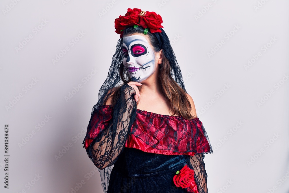 Young woman wearing day of the dead costume over white looking confident at the camera smiling with crossed arms and hand raised on chin. thinking positive.