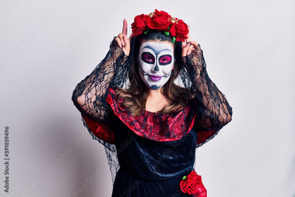Young woman wearing day of the dead costume over white posing funny and crazy with fingers on head as bunny ears, smiling cheerful