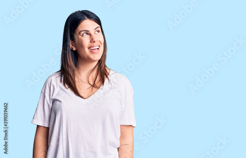 Young beautiful brunette woman wearing casual t-shirt looking away to side with smile on face, natural expression. laughing confident.