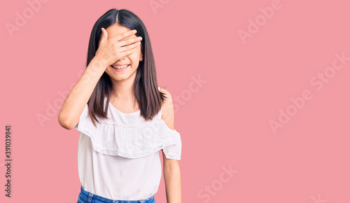 Beautiful child girl wearing casual clothes smiling and laughing with hand on face covering eyes for surprise. blind concept.
