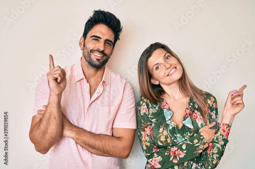 Beautiful young couple of boyfriend and girlfriend together with a big smile on face, pointing with hand and finger to the side looking at the camera.