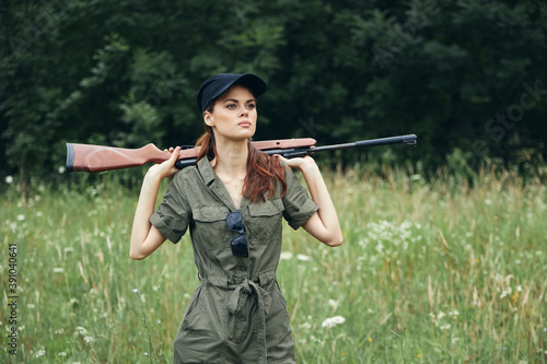 Woman holding a gun behind his back green jumpsuit hunting lifestyle black cap 