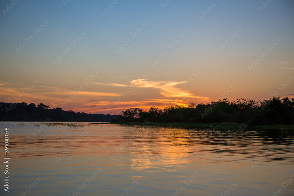 Stunning Amazon River sunset with the sun setting into the jungle horizon behind trees of the forest & reflecting into the Amazonian water in the State of Amazonas, Brazil, South America