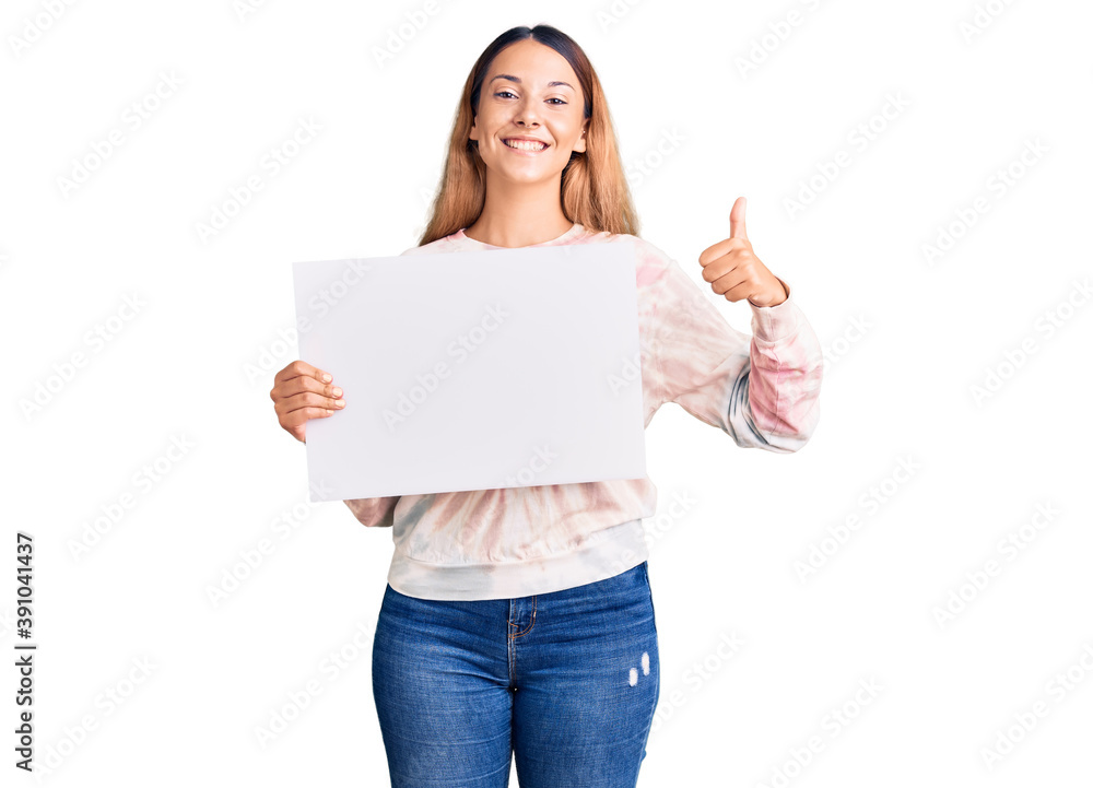 Beautiful young woman holding blank empty banner smiling happy and positive, thumb up doing excellent and approval sign Beautiful young woman holding blank empty banner smiling happy and positive, thumb up doing excellent and approval sign