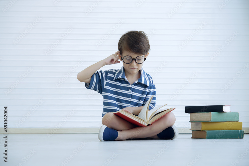 A little Caucasian boy wear eye glasses reading a book and thinking while sitting on the floor at home. Education kid and self learning at home concept A little Caucasian boy wear eye glasses reading a book and thinking while sitting on the floor at home. Education kid and self learning at home concept