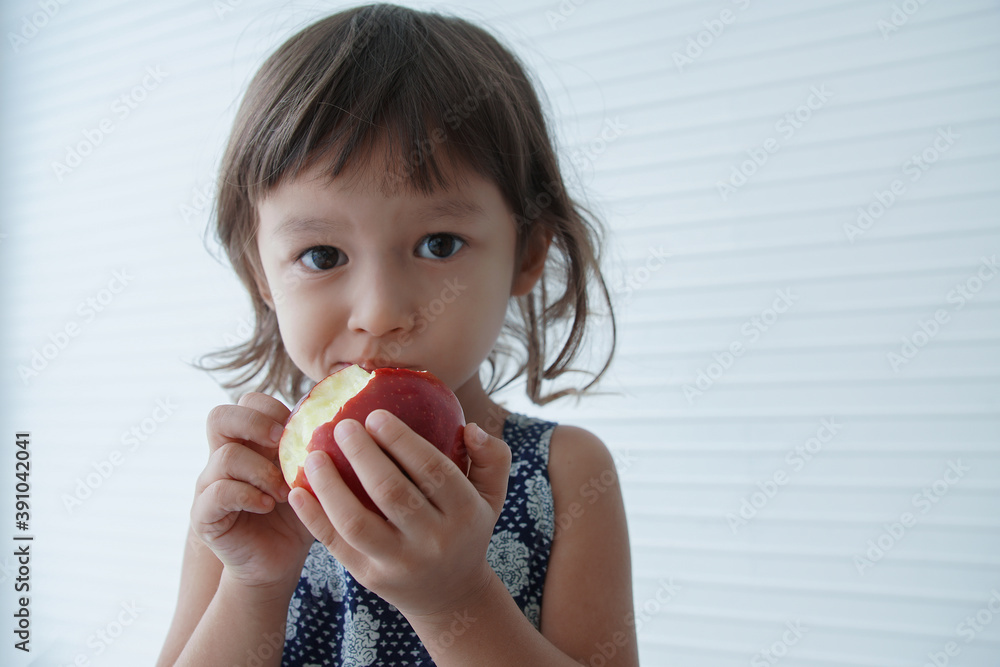 Portrait of little Caucasian girl holding and eating a big red apple in her hand on white background Portrait of little Caucasian girl holding and eating a big red apple in her hand on white background