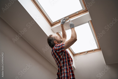 Young caucasian worker screwing skylight window handle photo