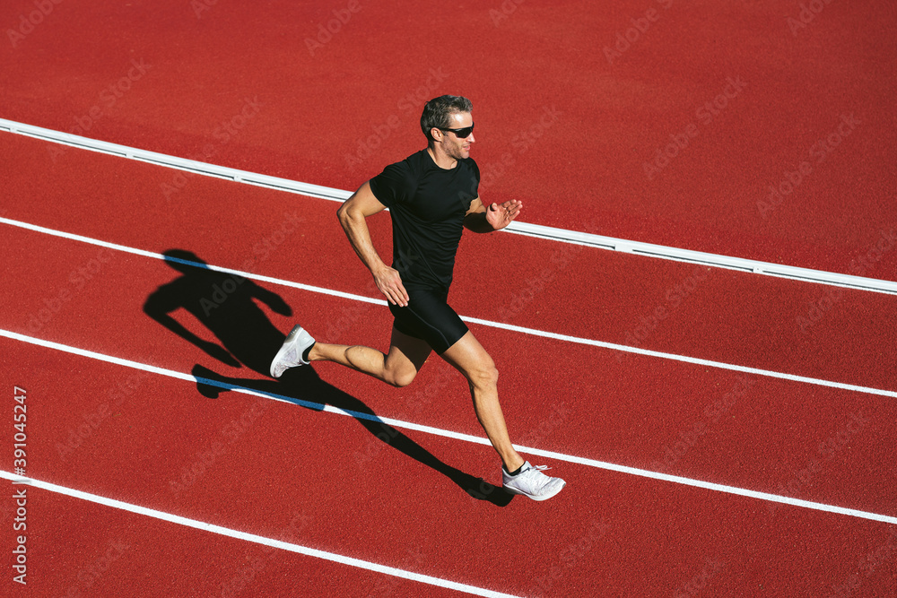 Mature fitness man with glasses running on the red running track. Copy space. Lifestyle and sports Mature fitness man with glasses running on the red running track. Copy space. Lifestyle and sports