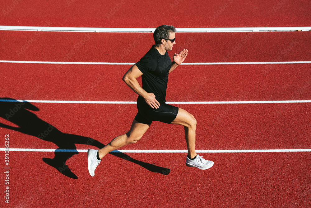 Mature fitness man with glasses running on the red running track. Copy space. Lifestyle and sports