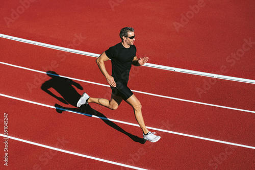 Mature fitness man with glasses running on the red running track. Copy space. Lifestyle and sports