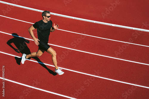 Mature fitness man with glasses running on the red running track. Copy space. Lifestyle and sports