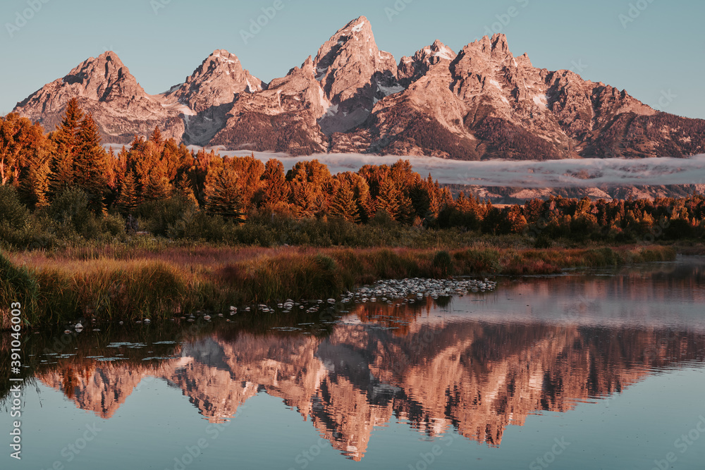 Obraz premium Sunrise glow hits the peaks and trees of the Teton Range of the Rocky Mountains. Schwabacher Landing in Grand Teton National Park, WY, USA. Water reflections of the Teton Range on the Snake River.