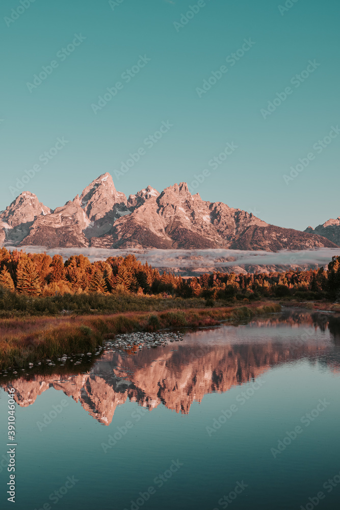 Sunrise glow hits the peaks and trees of the Teton Range of the Rocky Mountains.  Schwabacher Landing in Grand Teton National Park, WY, USA. Water reflections of the Teton Range on the Snake River. 