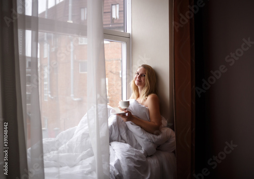 woman wrapped in a blanket sits on the windowsill by a large window Free Download woman wrapped in a blanket sits on the windowsill by a large window - GFXLoad