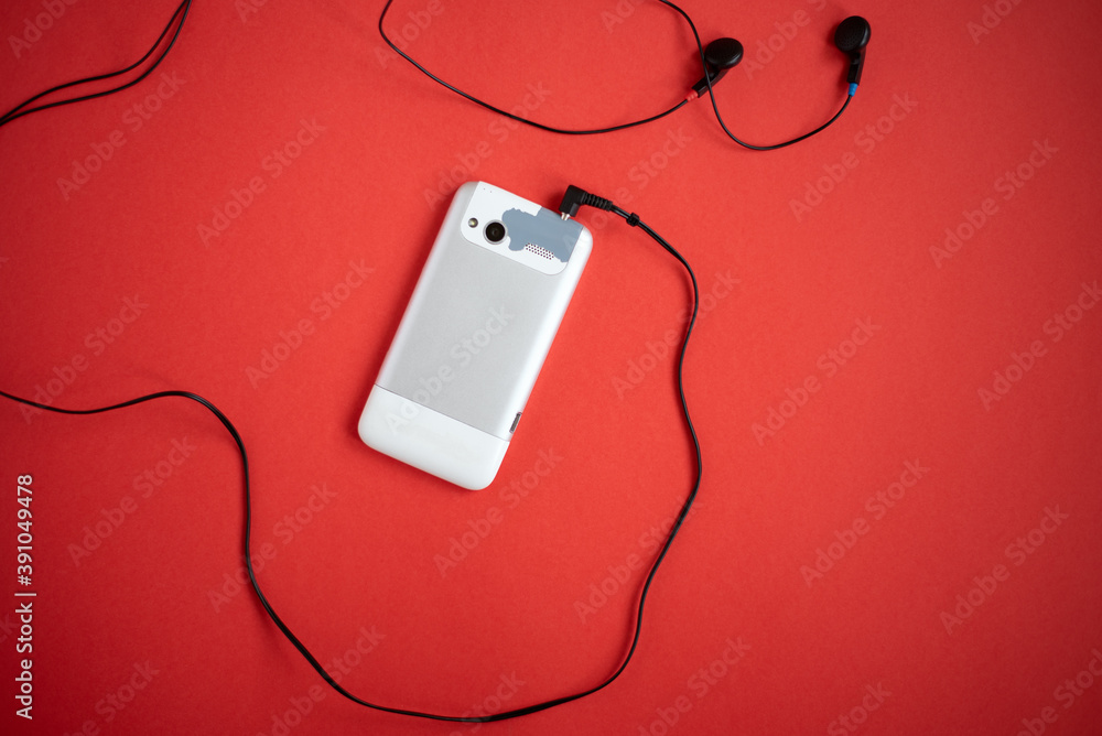 Old, outdated and worn cell phone and wired earbuds on a red background. Old, outdated and worn cell phone and wired earbuds on a red background.