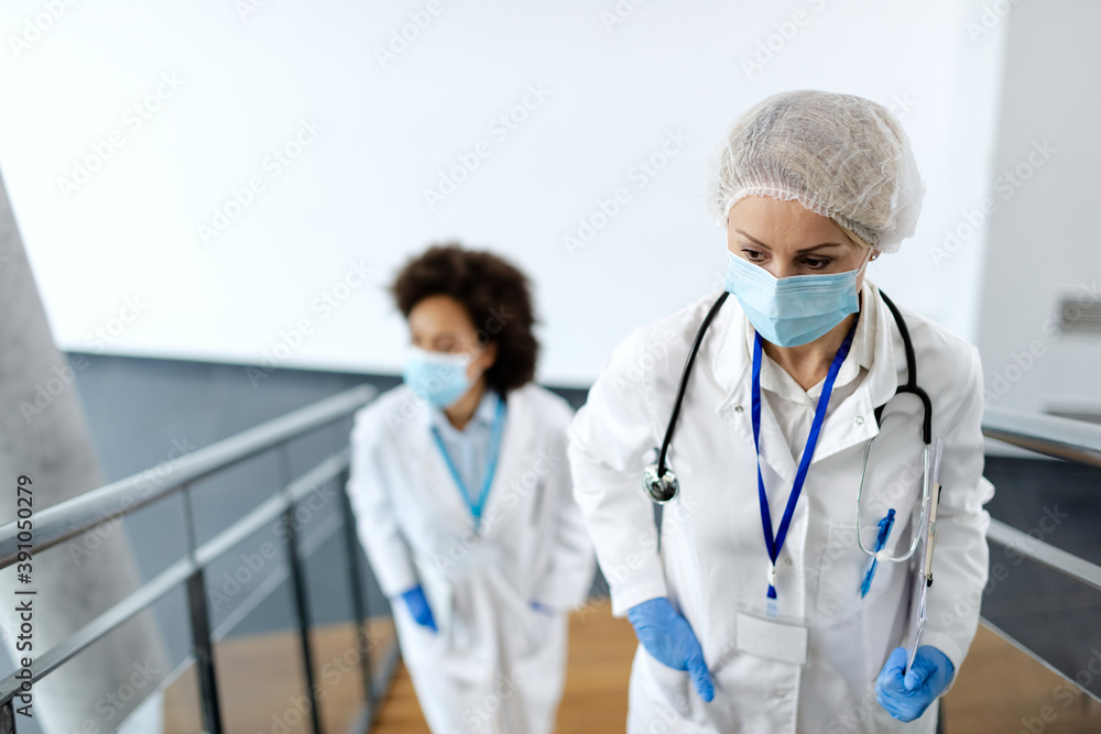 Distraught female doctor with face mask walking up the stairs at medical clinic.