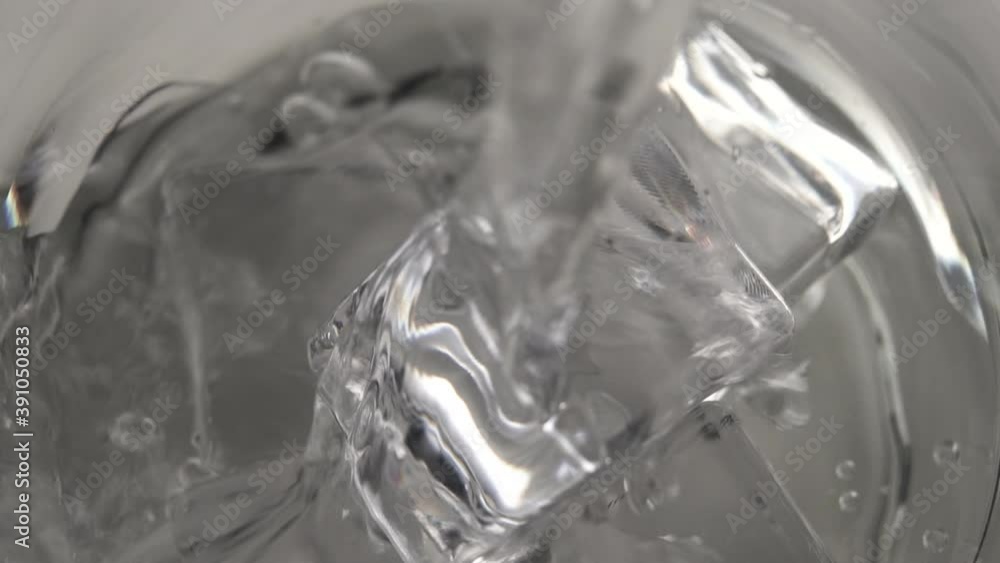 stream of pure water is poured into a glass with ice cubes. Slow motion. Macro shot