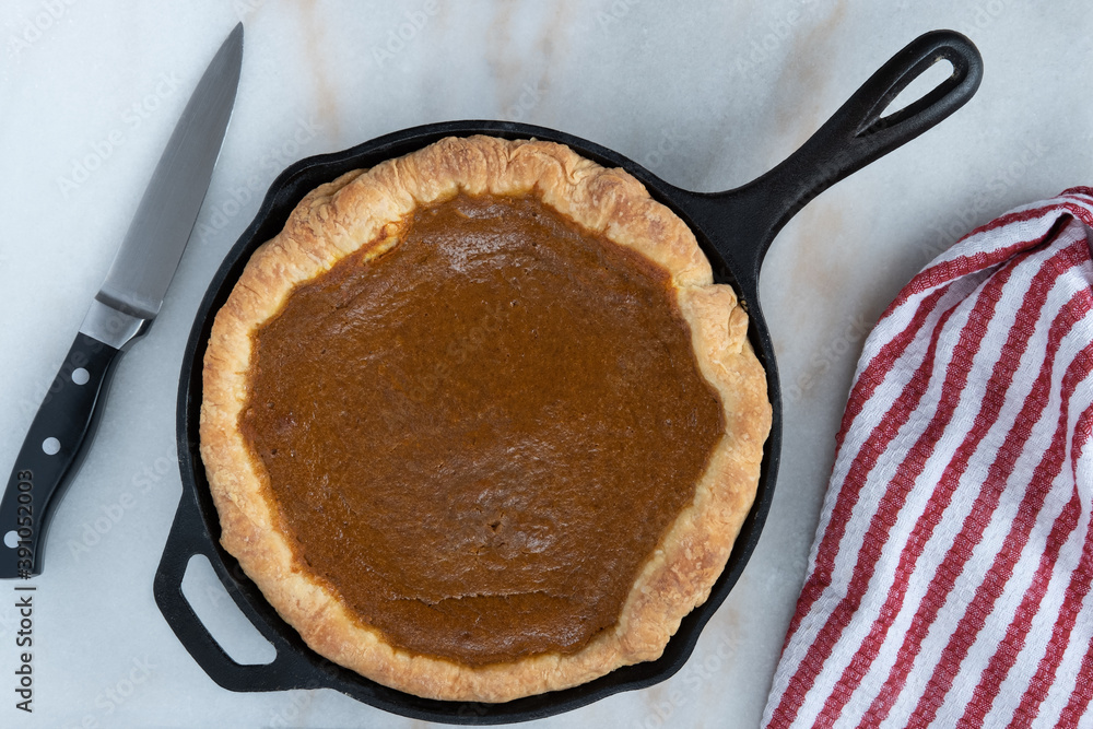 Fresh homemade pumpkin pie baked in a cast iron skillet on a kitchen counter with a knife and towel