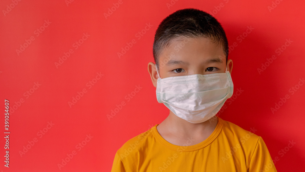 A boy in Thailand wears a COVID-19 virus mask and the dust is watching. Interior red wall background, New Normal A boy in Thailand wears a COVID-19 virus mask and the dust is watching. Interior red wall background, New Normal