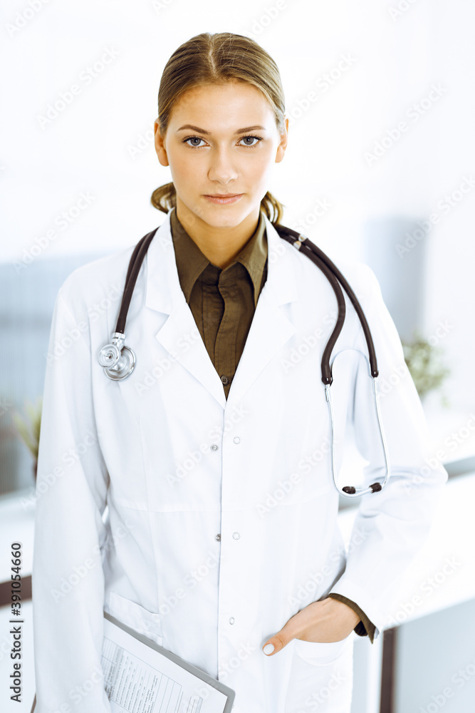 Woman-doctor standing and looking at camera. Perfect medical service in clinic Woman-doctor standing and looking at camera. Perfect medical service in clinic