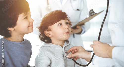 Doctor-woman examining a child patient by stethoscope in sunny clinik. Cute arab boy and his brother at physician appointment