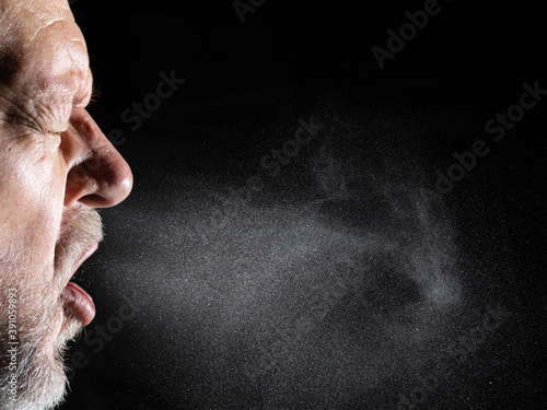 A man sprays aerosols into the air while speaking. The background is black. photo