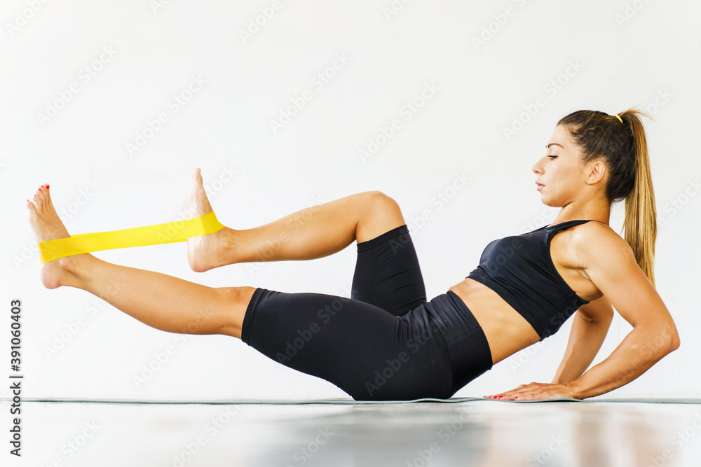 Side view full length on adult caucasian woman fitness instructor training on her abs muscles - sporty female crunches on the floor fitness mat exercise with rubber resistance band