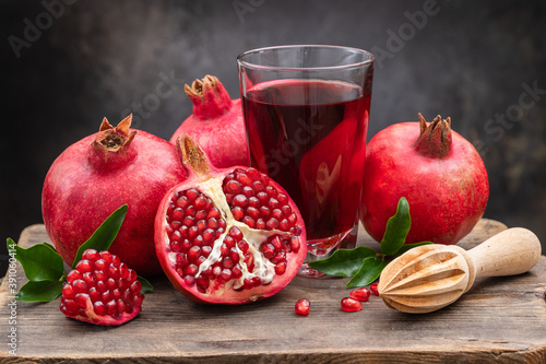 Ripe pomegranate, half a juicy pomegranate and healthy pomegranate juice in a glass on a cutting board, side view, dark vintage background. photo